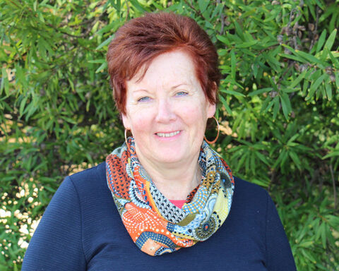 Women wearing multi colour scarf standing behind greenery