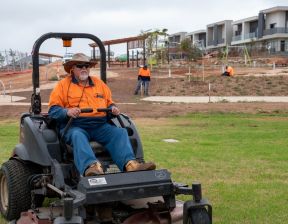 Man wearing orange top, bucket hat and sunglasses sitting on mower