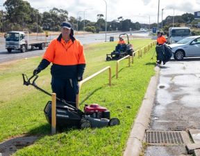 Large patch of green lawn area with people doing work, two of them with mowers