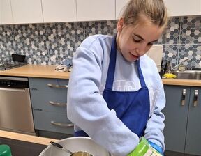 Women wearing blue colour apron adding in cheese to a bowl