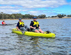 Two men sitting in neon yellow kayak and hats kayaking in water