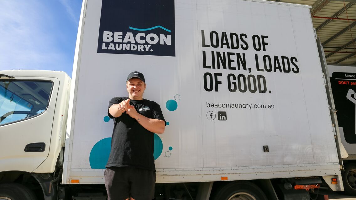 Man wearing cap and standing in front of white colour truck with beacon laundry logo and tagline