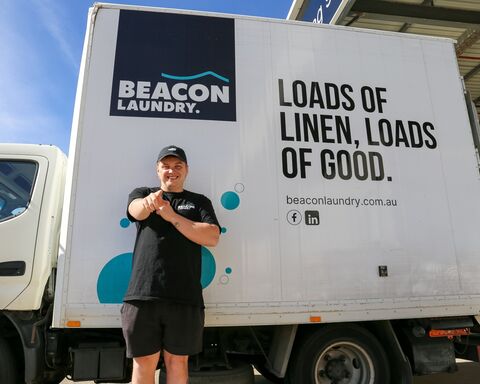 Man wearing cap and standing in front of white colour truck with beacon laundry logo and tagline
