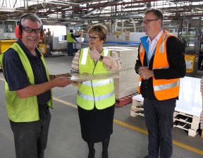 Three individuals wearing hi-vis vests standing in a factory