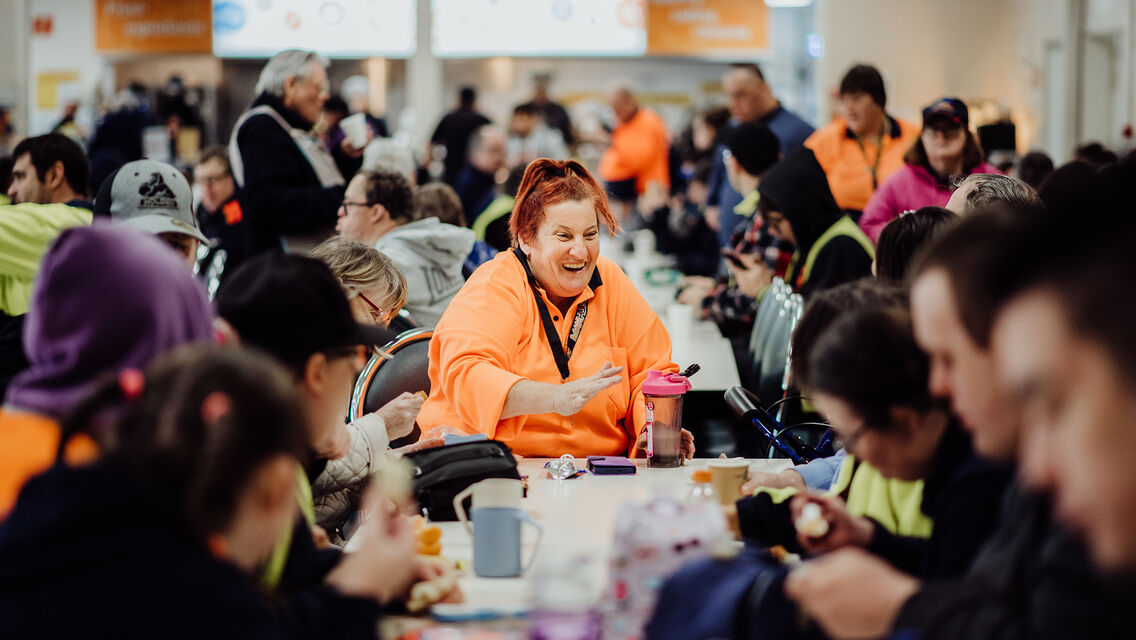 Group of people sitting in the cafe, eating, talking with each other. Lady in orange hi-vis outfit
