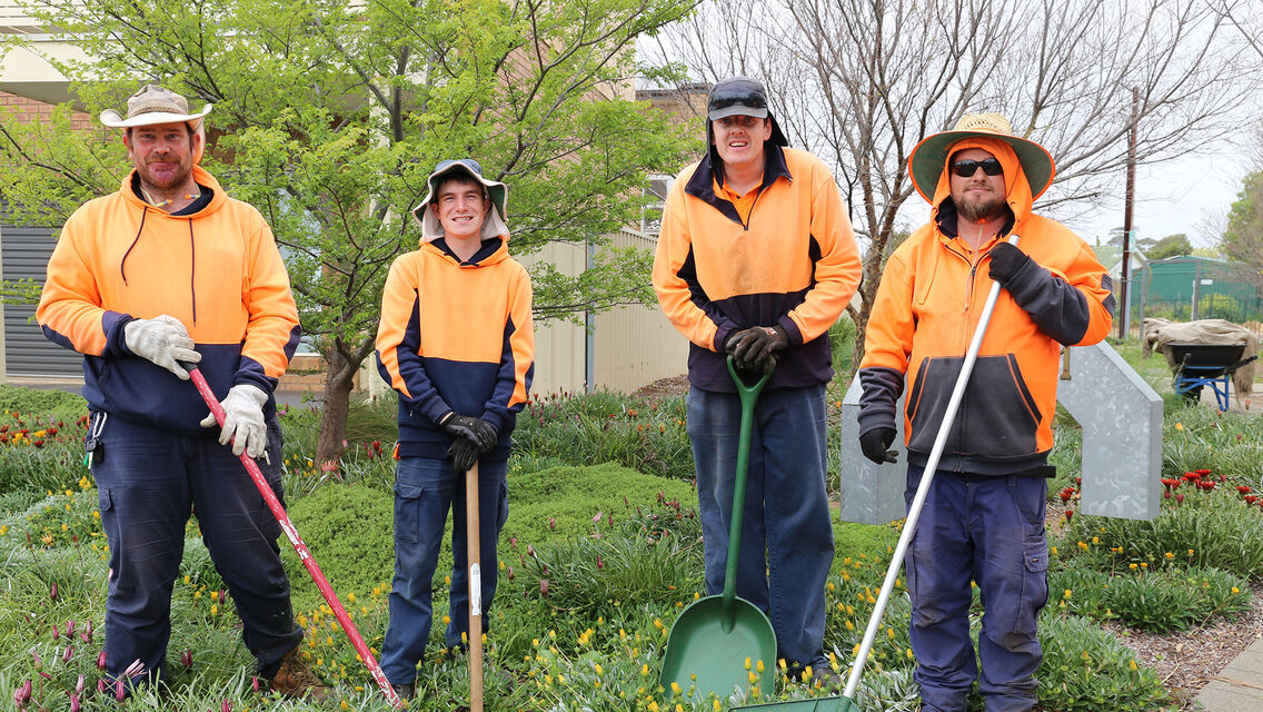 Four individuals wearing hi-vis orange colour clothing with gardening equipment in their hands