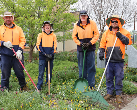 Four individuals wearing hi-vis orange colour clothing with gardening equipment in their hands