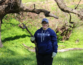 Women wearing blue colour jumper and gloves holding a tree branch in hand