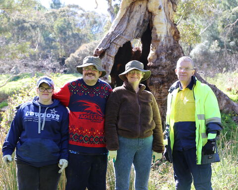 Four individuals standing next to each other outdoors and smiling at camera