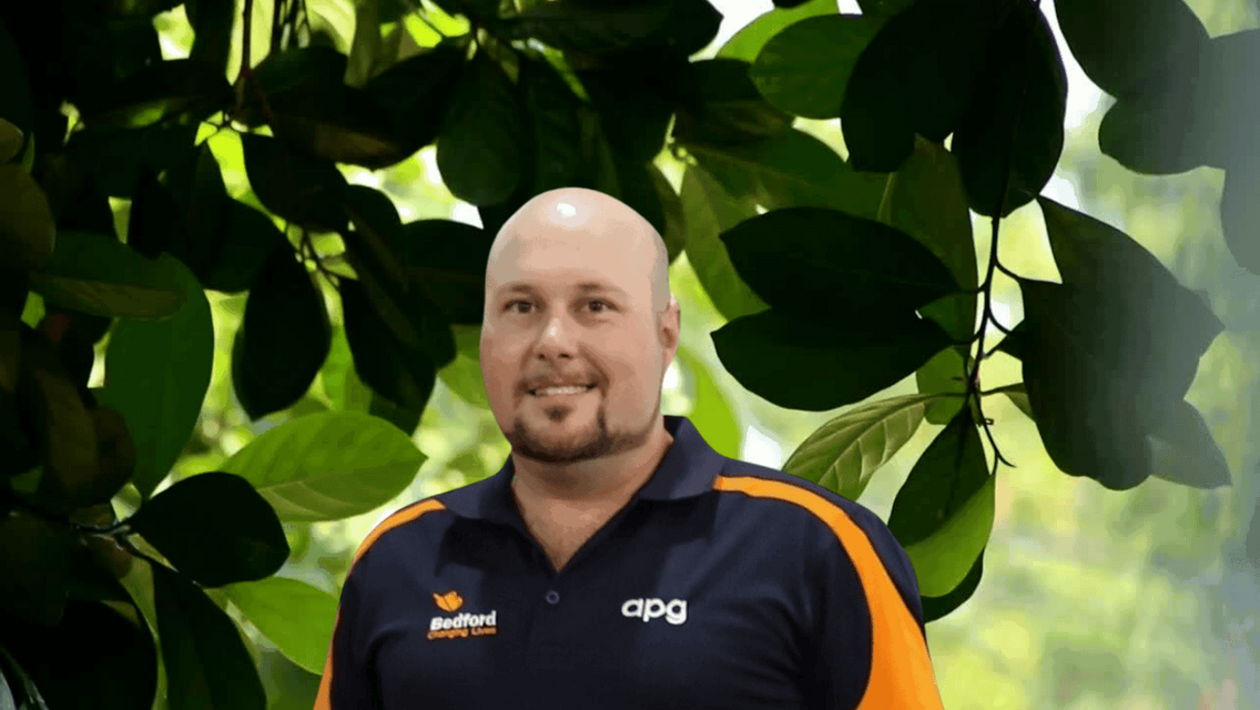 Man wearing Apg polo standing behind green leaves