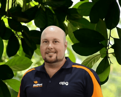 Man wearing Apg polo standing behind green leaves