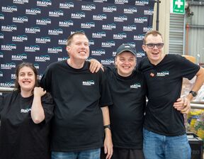 Four individuals wearing black t-shirt standing and smiling