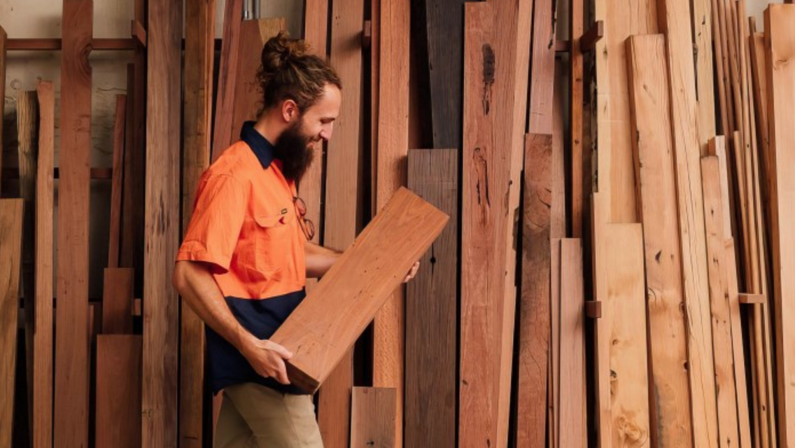 Man wearing orange hi vis clothing holding a log of wood
