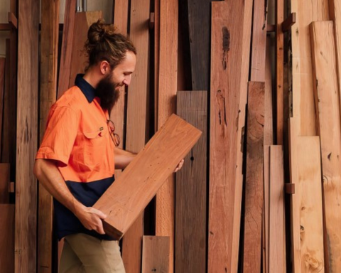 Man wearing orange hi vis clothing holding a log of wood