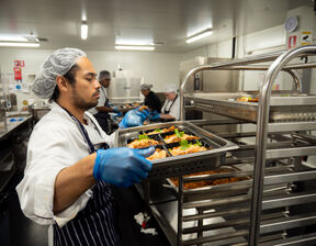 Person wearing apron stacking tray of food shelves