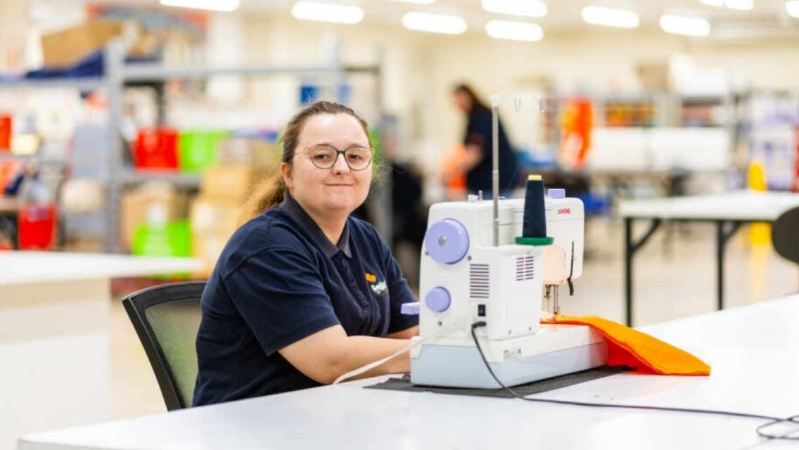 Women wearing navy blue polo sitting next to a white colour sewing machine