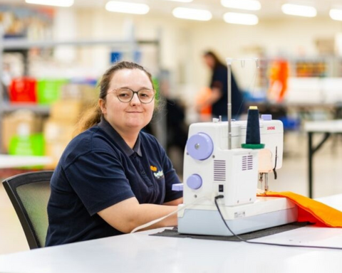 Women wearing navy blue polo sitting next to a white colour sewing machine