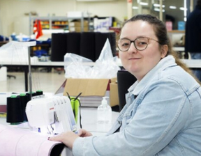 Women wearing specs and light blue denim jacket sitting next to sewing machine