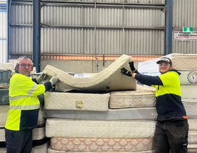 Two men holding mattresses looking at camera