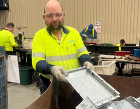 Man wearing hi-vis polo with protective glasses holding discarded electronics