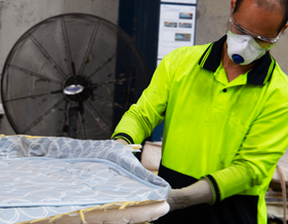 Man wearing hi-vis yellow polo t shirt with face mask cutting mattresses