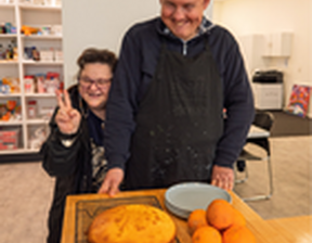 Man and women standing next to each other with a cake and oranges on the table
